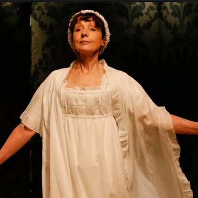 Woman wearing a Regency gown, cap and wrap, with arms outstretched.