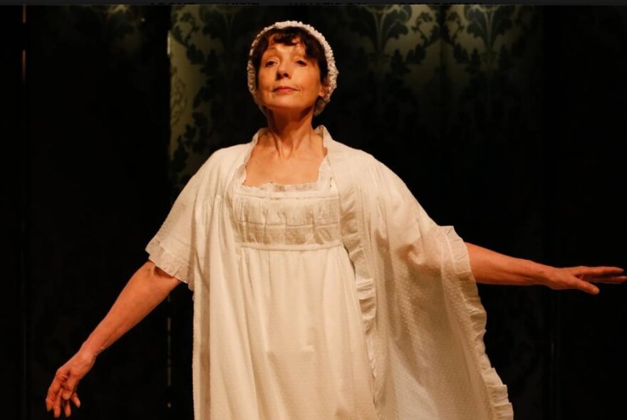 Woman wearing a Regency gown, cap and wrap, with arms outstretched.