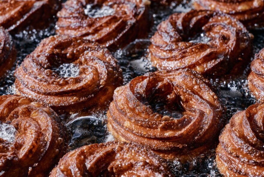 Crullers, made from deep-fried choux pastry, cooking in oil in a deep fryer.