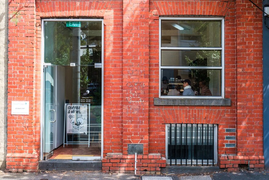 A cafe with a brick exterior. There is a sign at the doorway saying coffee and vinyl.
