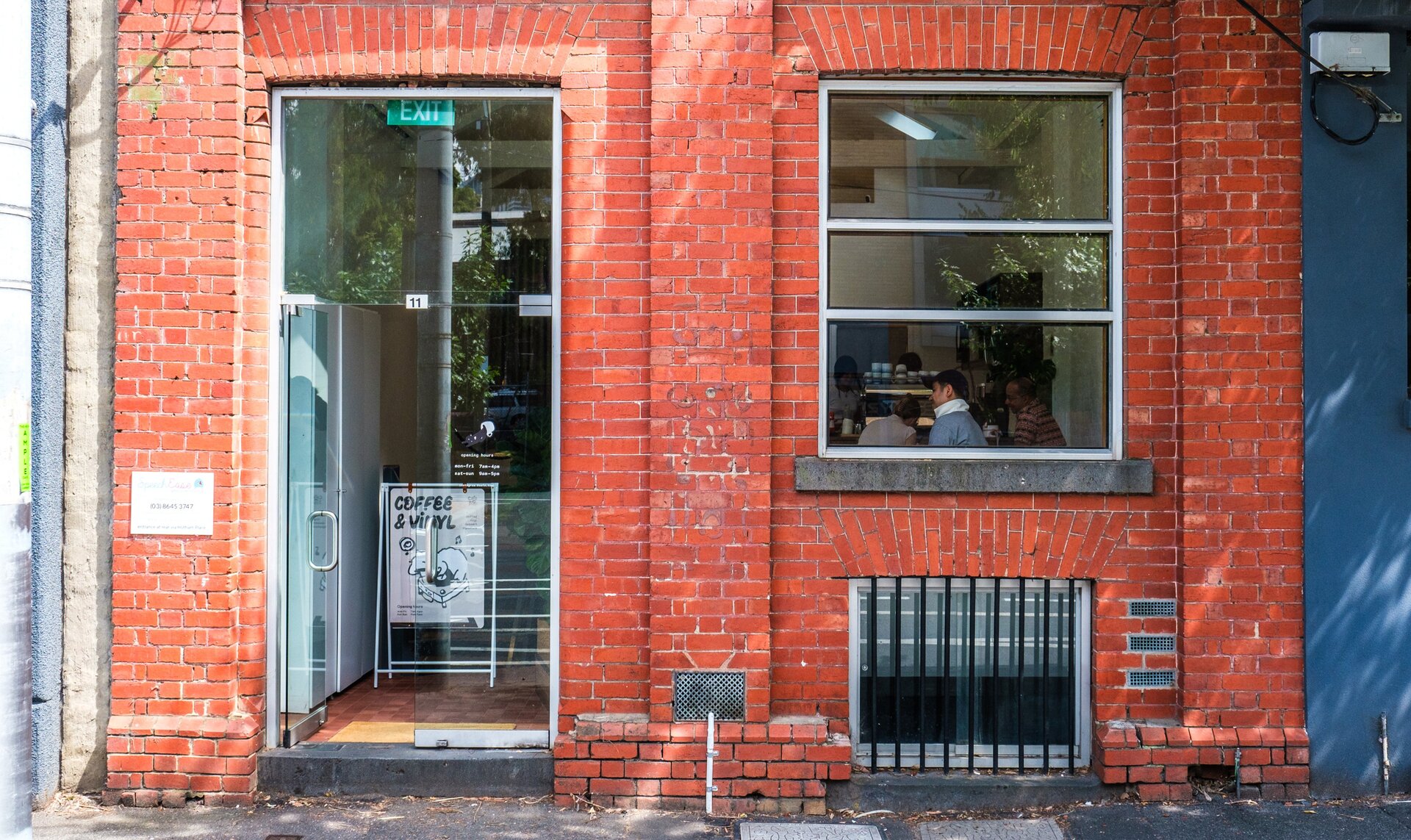 A cafe with a brick exterior. There is a sign at the doorway saying coffee and vinyl.