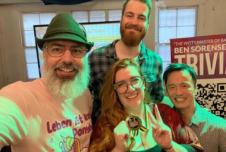 Four people looking happy, one holding a medal and giving a peace sign, one wearing a Tyrolean hat.