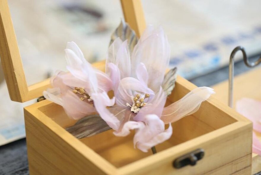 A wooden display case showcasing a delicate hand-made flower.