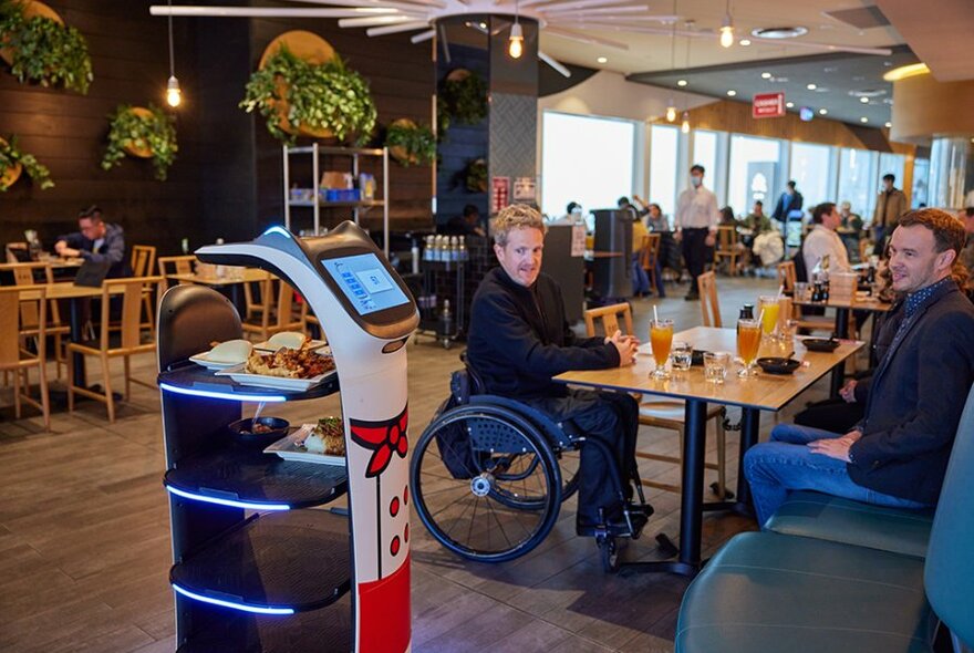 Diners looking at a robot waiter delivering food in a restaurant. 