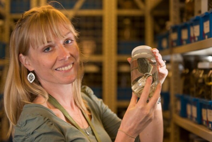 A woman holding up a glass jar containing a scientific specimen.