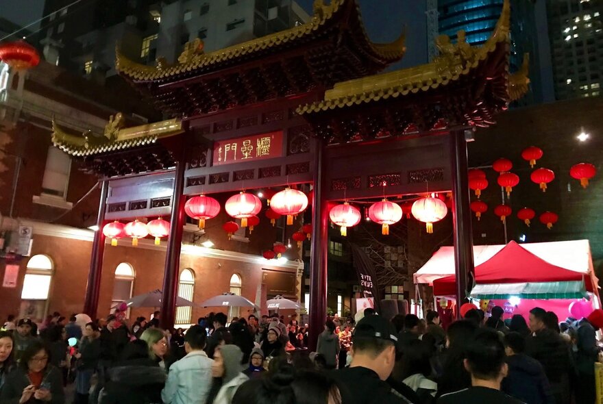 Outdoors at night at a Chinese festival with red lanterns and a traditional Chinese building. 