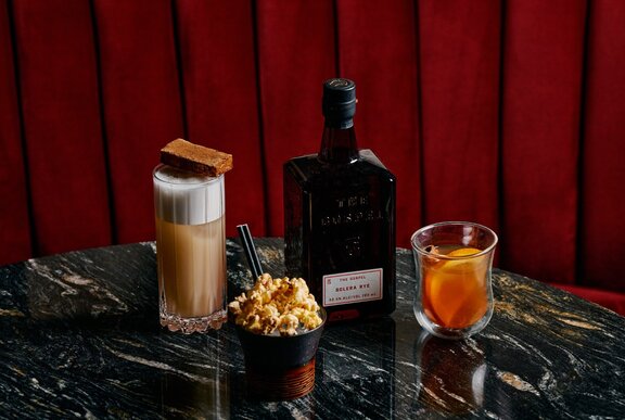 A dark marble table with several whiskey-based cocktails and a black whiskey bottle on top. 
