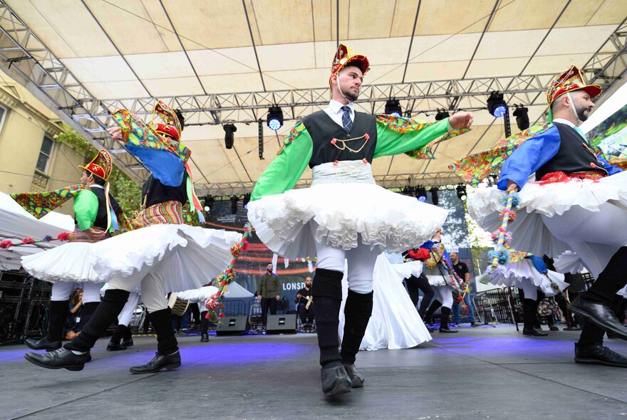 Greek dancers performing on a stage wearing skirts and boots.