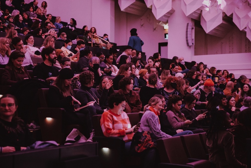 A seated theatre audience with house lights half on.