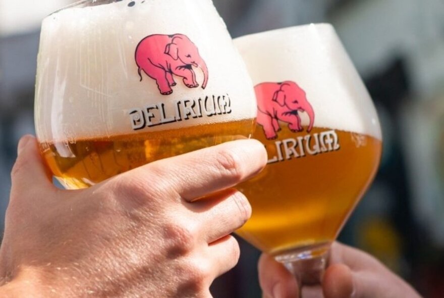 Hands clinking large glasses of beer with elephant logo.