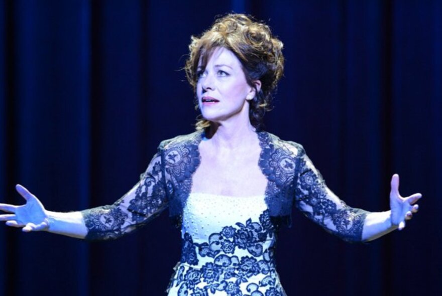 Performer wearing a lace formal dress, her hair tousled and arms outstretched.