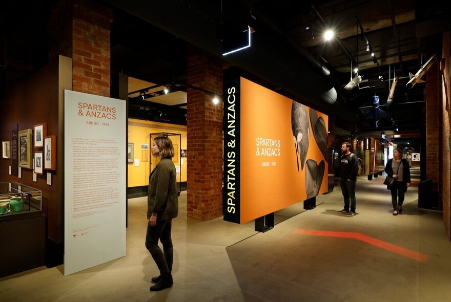 Installation view of the Spartans & Anzacs exhibition at the Shrine of Remembrance, with people walking around the space, reading panels and looking at displays.