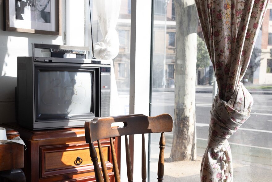 Retro cafe interior with old-style analogue TV set, wooden chair and knotted curtain.