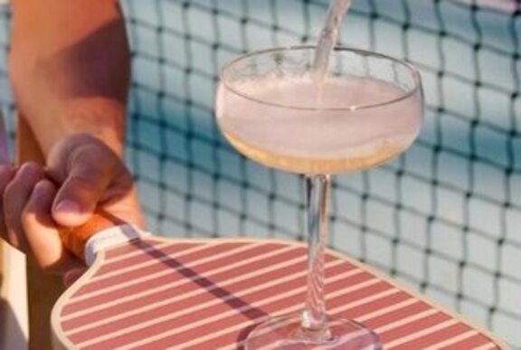 A wide champagne glass being filled as it rests on a pickleball paddle.
