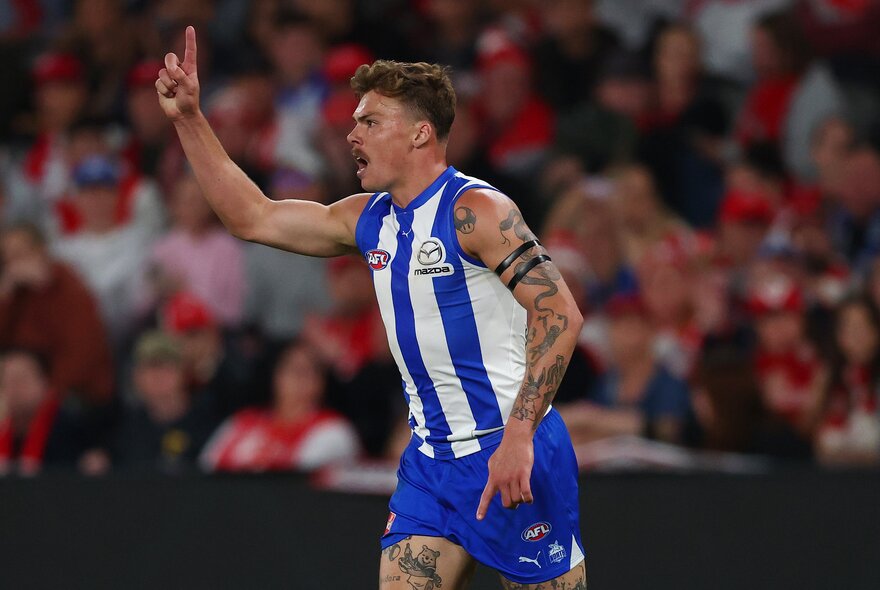 North Melbourne AFL football player with his arm raised in the air, and cheering, on the field during a match.