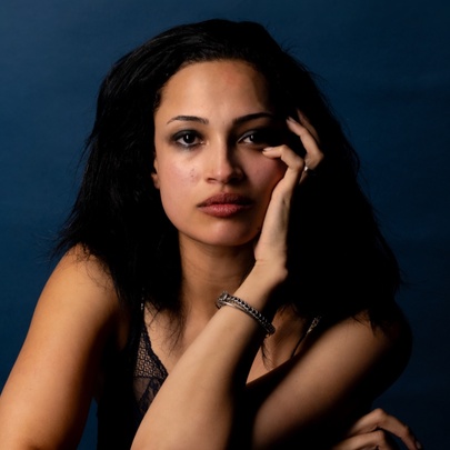 Actor Sarah Ruhl posing with her hand on her face and looking blankly ahead in a dark navy room. 