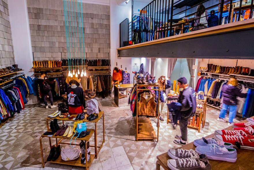 Inside a vintage clothing store with racks of clothes, shelves with shoes and people looking at racks of clothing