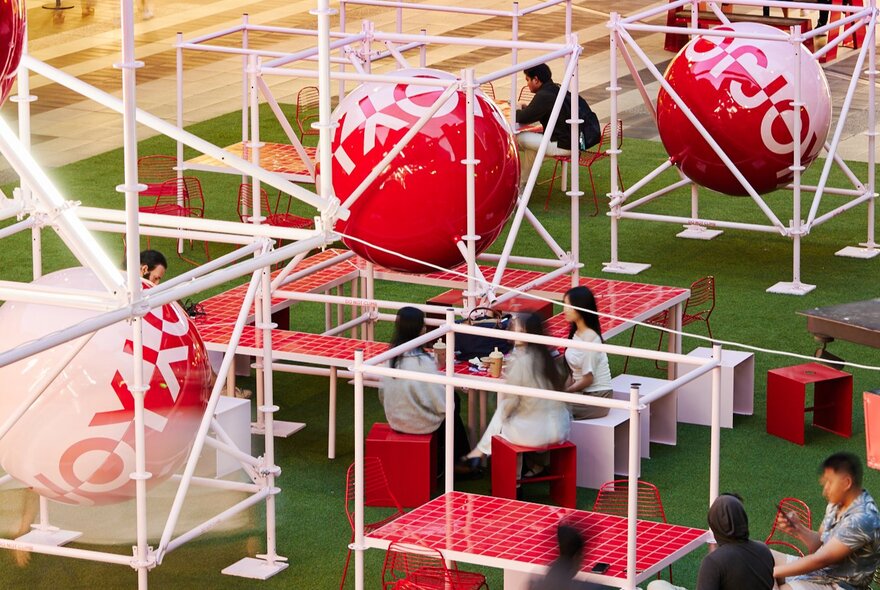 The QV Christmas tree installation of white empty cubes and oversized baubles, with people seated at chairs and tables on the AstroTurf.
