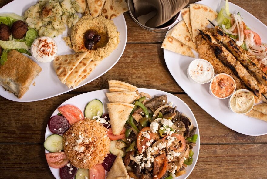 Looking down on plates of meat, pita bread with dips and mezze.