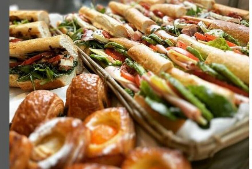 A tray of filled french baguettes next to a collection of Danish pastries and chocolate croissants.