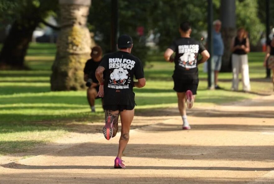 Two men running around Princes Park in Melbourne, both wearing black t-shirts that say, Run For Respect, on the back.