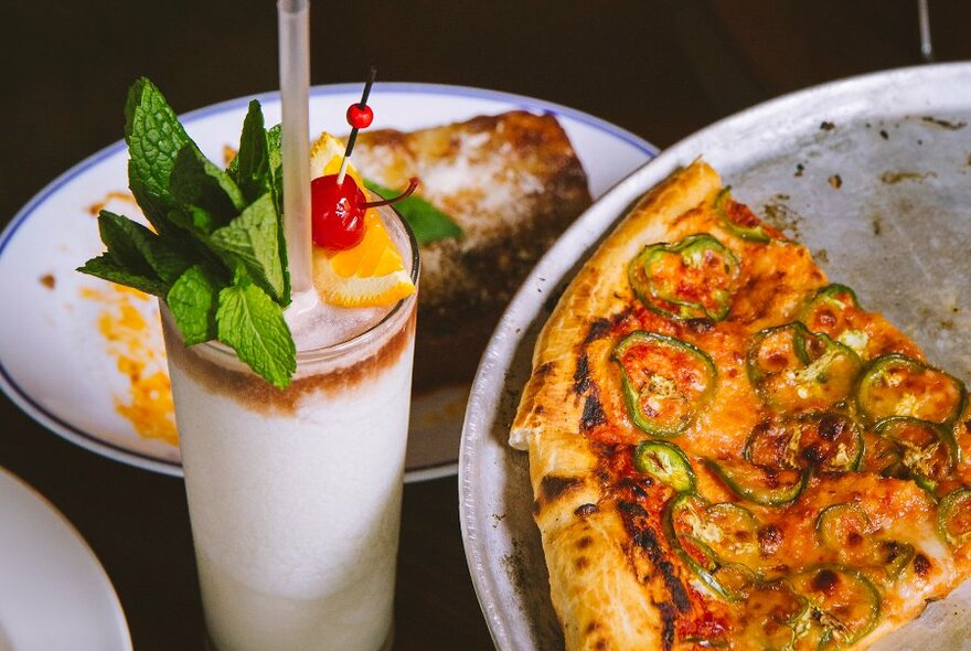 A tray of pizza and a pina colada topped with mint, orange and a cherry.