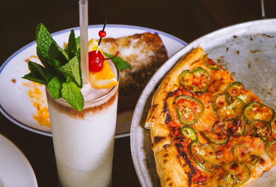 A tray of pizza and a pina colada topped with mint, orange and a cherry.