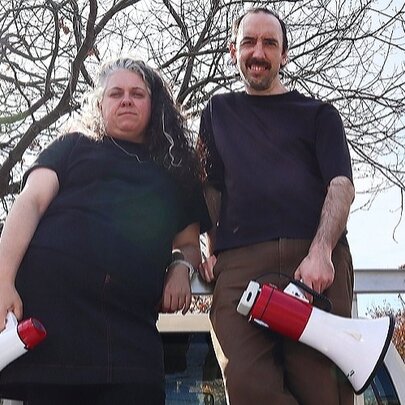 Two actors holding megaphones in front of bare trees.