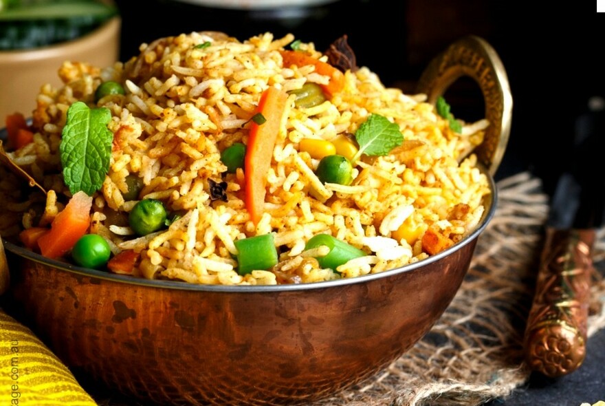 Copper dish full of rice and some vegetables.