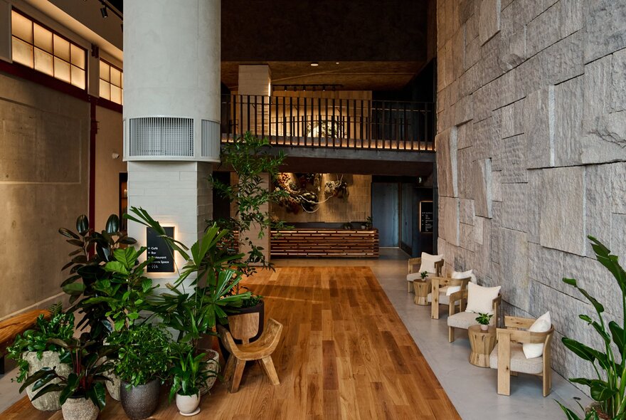 The spacious lobby of 1 Hotel Melbourne with warm timber floors, green potted plants and armchairs.