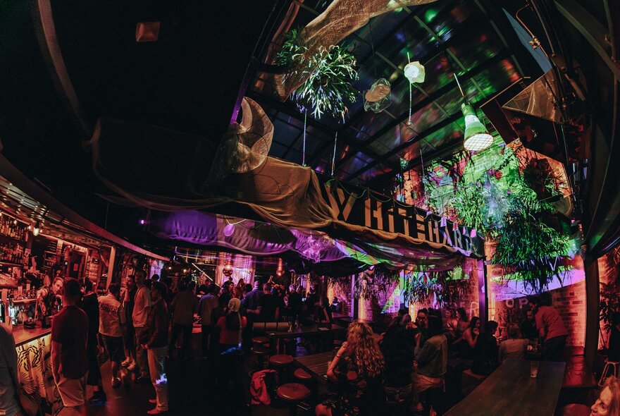 A crowd of people at night, seated and socialising at Whitehart Bar, a multi-level outdoor venue.