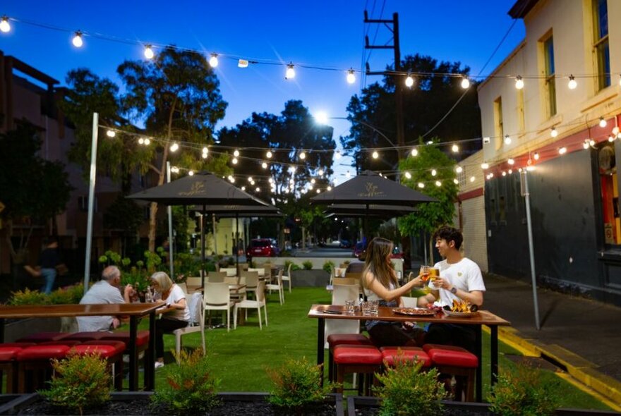 People seated outside in the evening enjoying drinks .