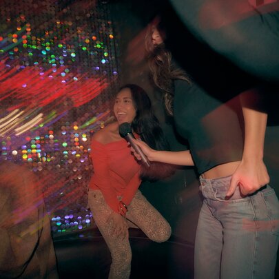 Blurred images of people singing and enjoying themselves at a karaoke bar, one person holding a microphone in front of her friend's face.