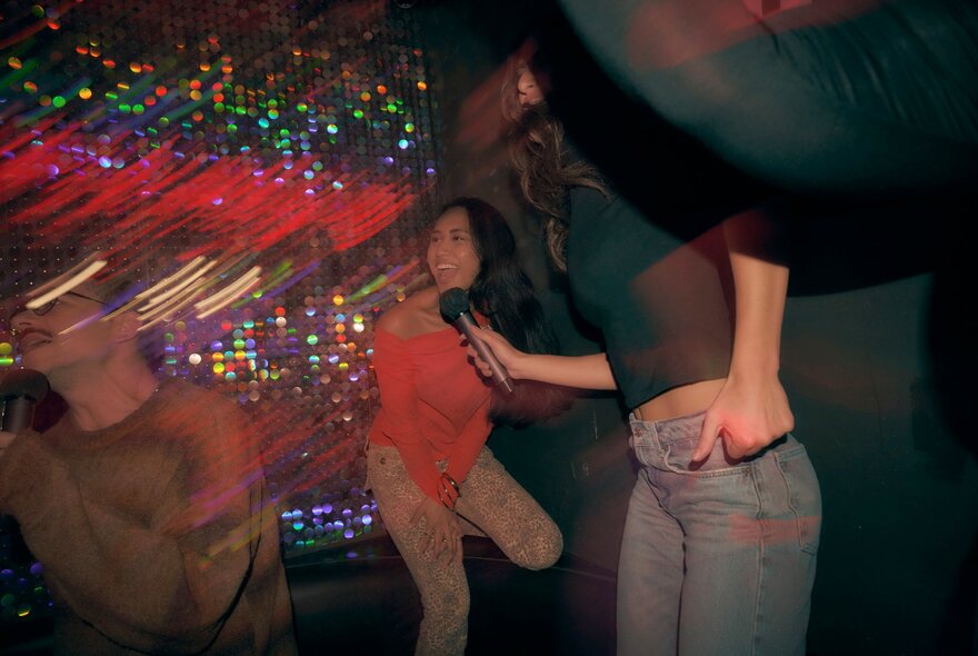 Blurred images of people singing and enjoying themselves at a karaoke bar, one person holding a microphone in front of her friend's face.