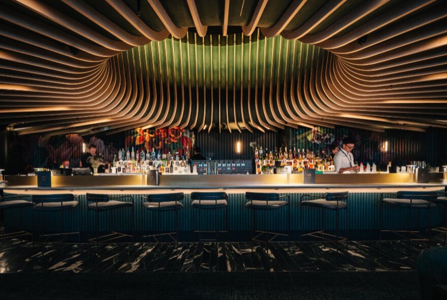 Dramatic sculptured ceiling of Amphora, with a bartender behind a dimly-lit bar with empty seats. 
