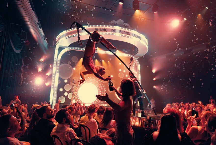 A cabaret show with a performer balancing on pole about to pour a bottle of champagne
