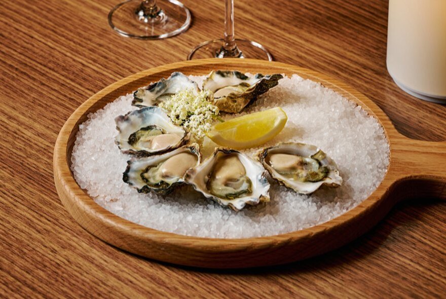 Natural oysters on a wooden serving platter filled with salt.