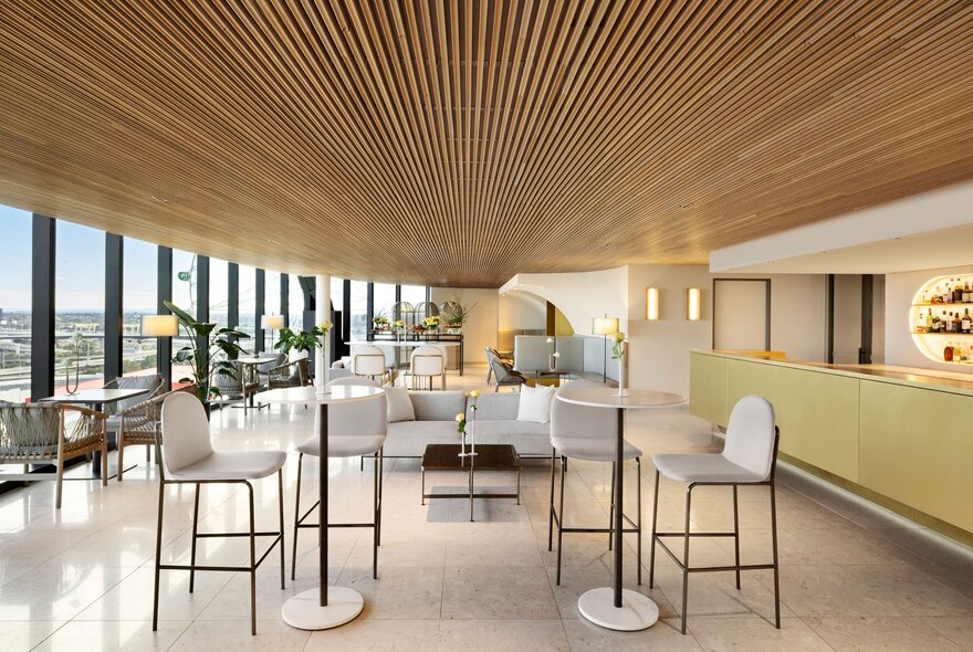 The minimalist interior of a modern restaurant with a wood-lined ceiling and floor-to-ceiling windows.