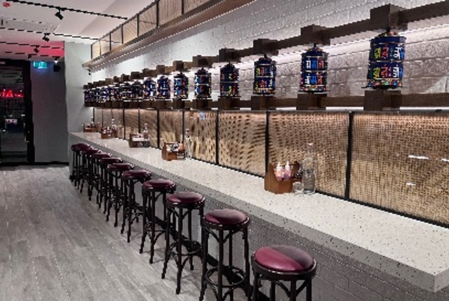 Restaurant interior counter area, with red cushioned stools underneath the counter.