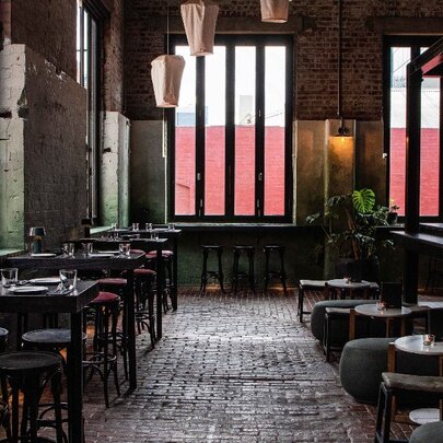 Interior of Longsong bar showing cobbled floor, small tables and chairs perched near large windows, hanging lanterns and greenery.