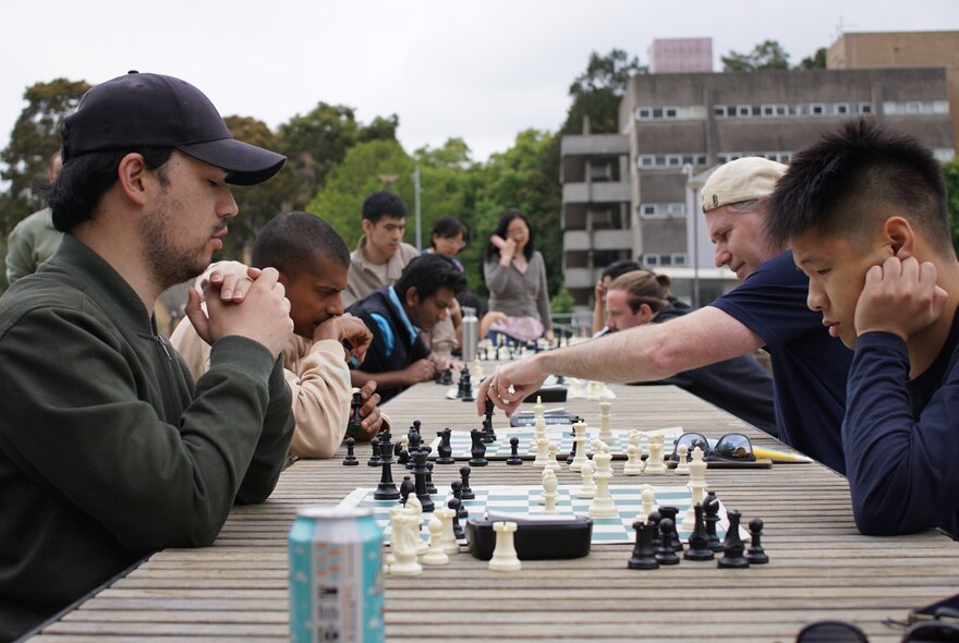 People facing each other across a table outdoors in an open square, playing chess.