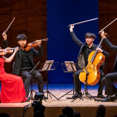 Four young members of a chamber music group performing on stage with batons in the air. 