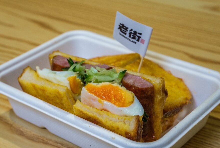 A takeaway box filled with a Taiwanese breakfast sandwich of egg and sausage.