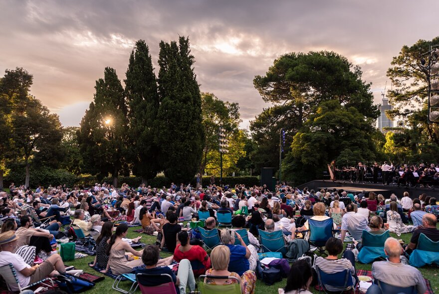 People seated on a large lawn at dusk in a public garden. 