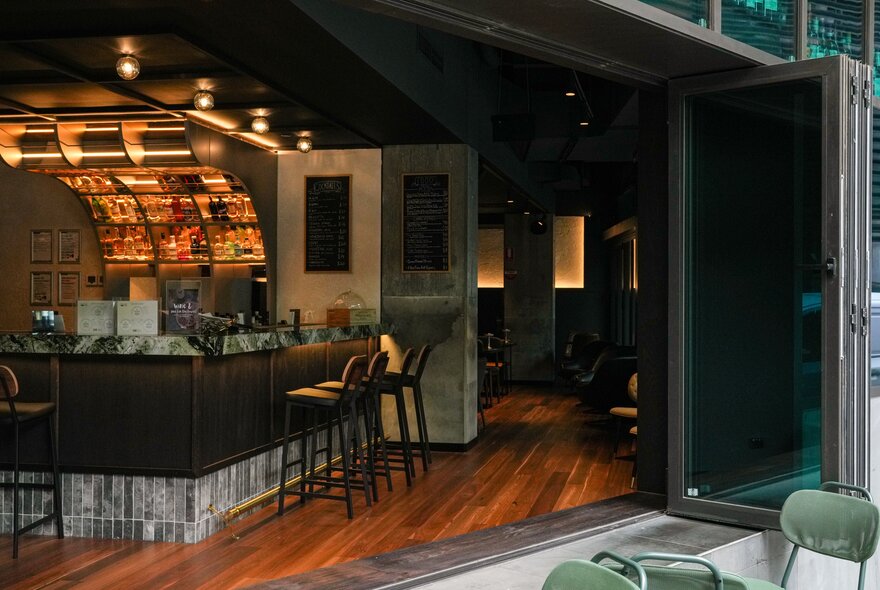 Inside a dimly lit bar showing folding doors that are wide open. 