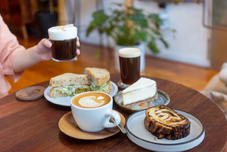 A table with three different types of coffee, two cakes and a sandwich 