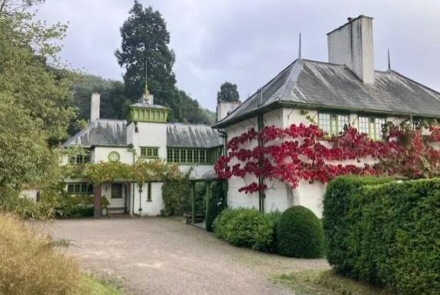 Arts and crafts home with ivy-covered walls, turret and gardens.