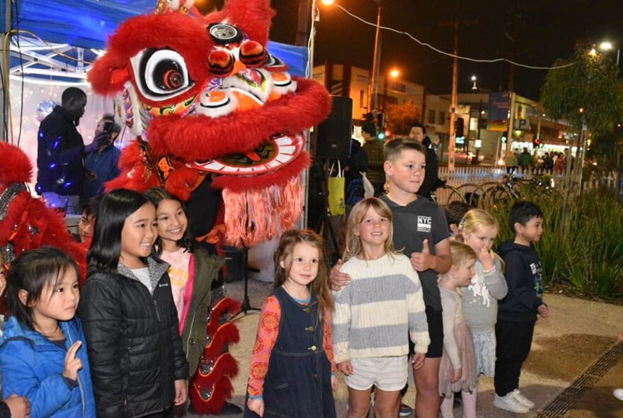 A row of smiling young children lined up and posing for a photograph in front of a large Chinese dragon puppet.