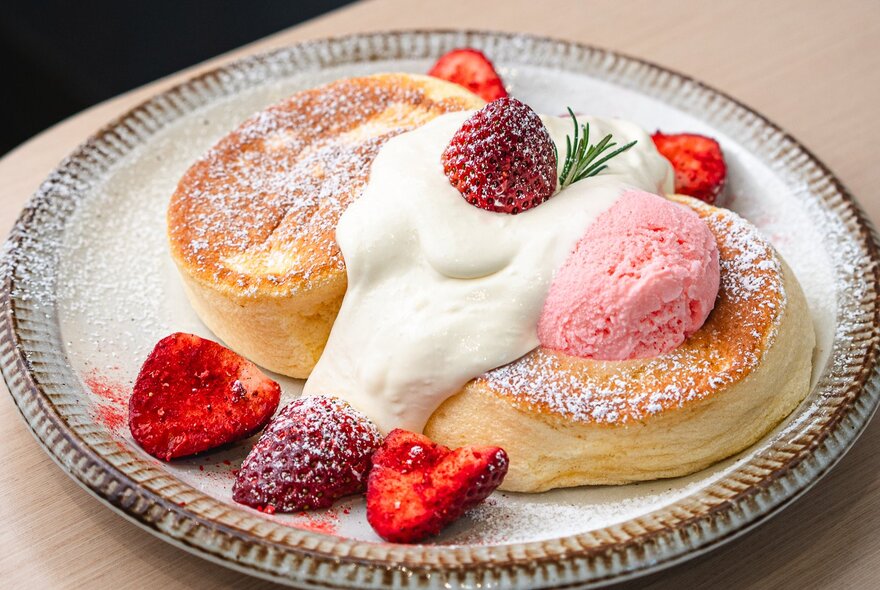 Two souffle-style fluffy pancakes on a plate topped with ice-cream, berries and dusted with icing sugar.