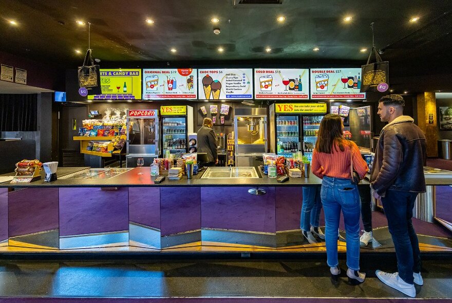 A couple ordering at the candy bar at a movie theatre.